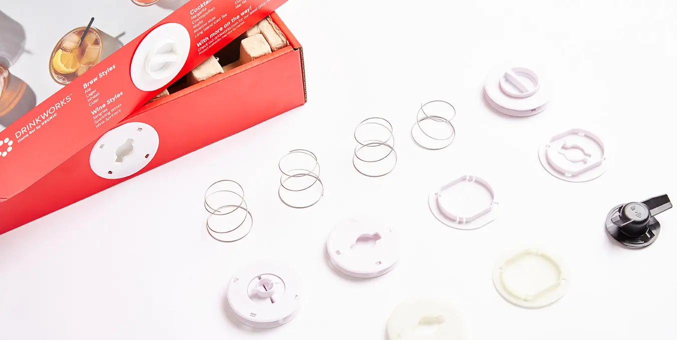 Detailed array of Drinkworks interactive switcher parts, neatly arranged beside the vibrant packaging