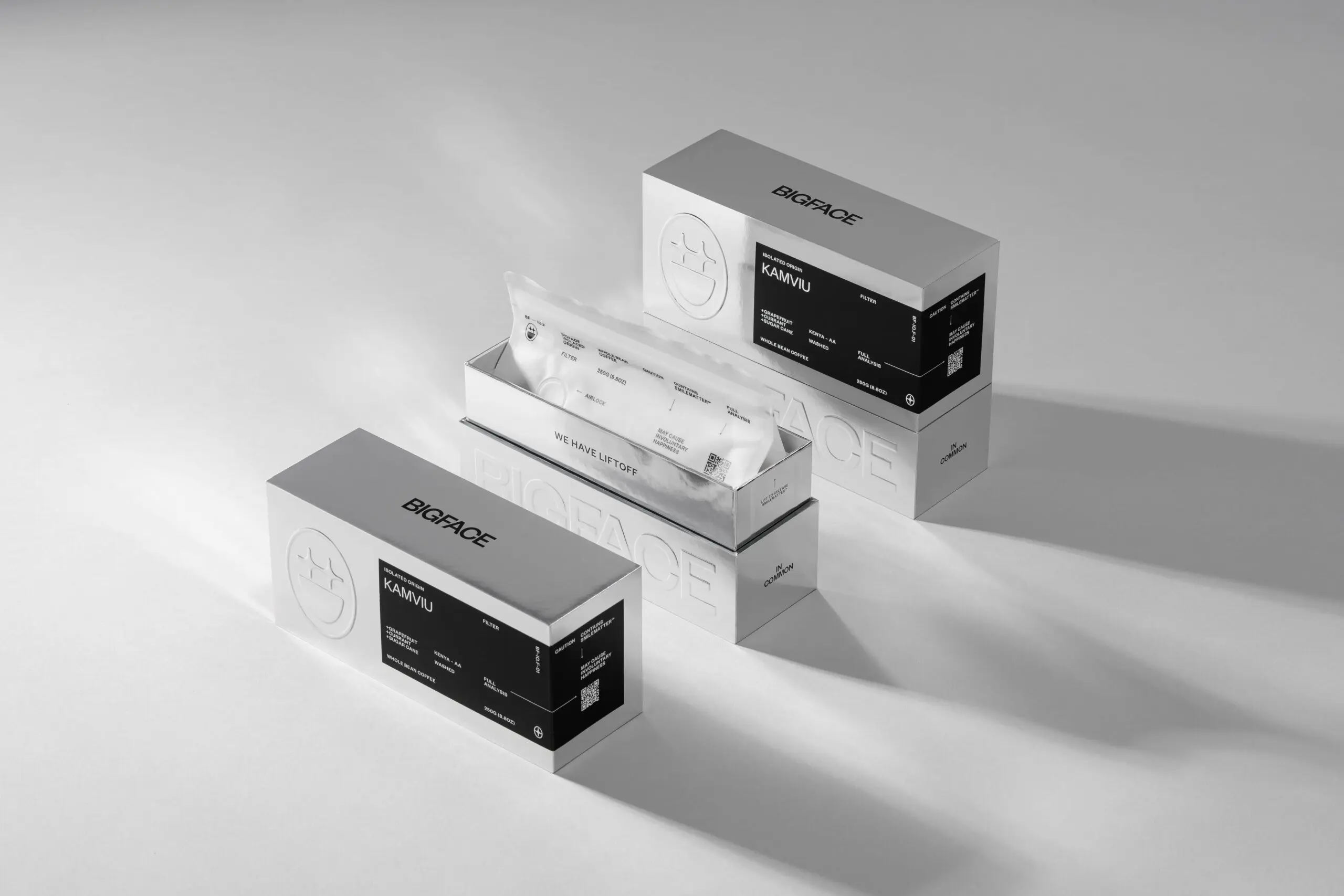 Three BIGFACE Brand coffee boxes featuring minimalist silver sleeves with black labels, showing one open box revealing a white coffee bean pouch labeled "WE HAVE LIFTOFF."