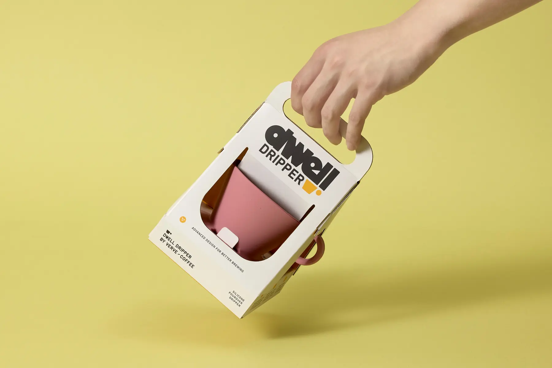 Hand holding Dwell Dripper coffee packaging designed by Zenpack, featuring die-cut window displaying pink pour-over dripper and top carry handle.
