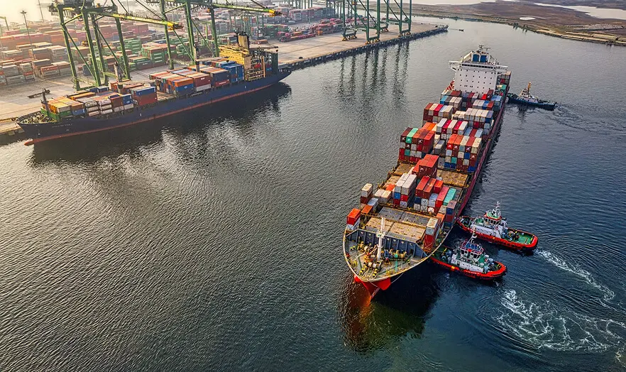 Cargo ships guided by tugboats at a port for Zenpack international freight packaging services.