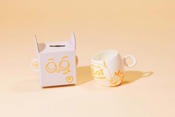 Brooklyn Robot Foundry mug beside whimsical packaging with playful faces, by Zenpack.
